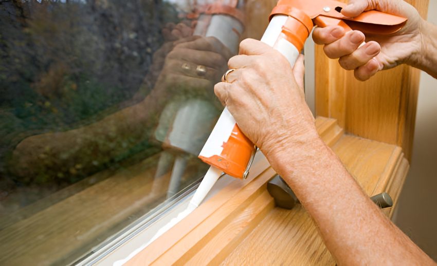 close-up of a man applying weather seal caulk to a window frame